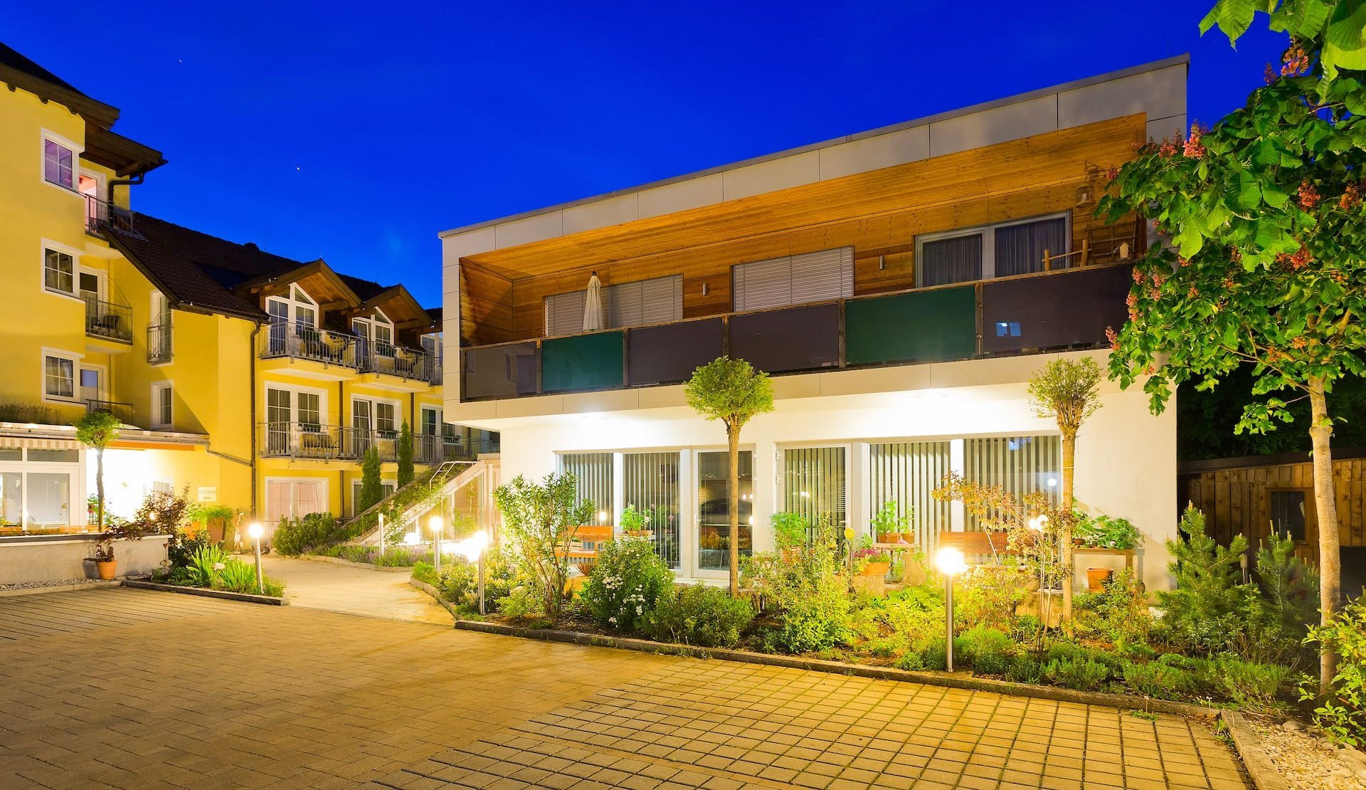 Moderne Außenansicht des Apartments im Hotel zum Mohren in Reutte mit idyllischem Garten und ruhiger Innenhoflage bei Dämmerung.
