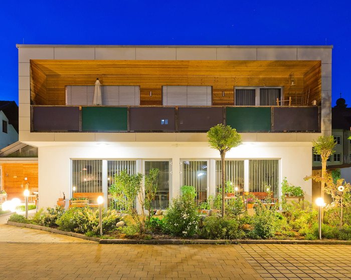 Frontale Ansicht des Apartments im Hotel zum Mohren mit stilvollem Holz-Balkon und beleuchteter Gartenterrasse zur blauen Stunde.